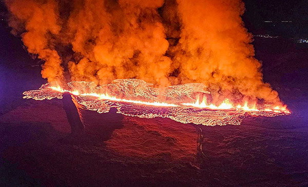 Orange smoke billows up from a fiery lava flow that slashes a line across the landscape in this nighttime photo.