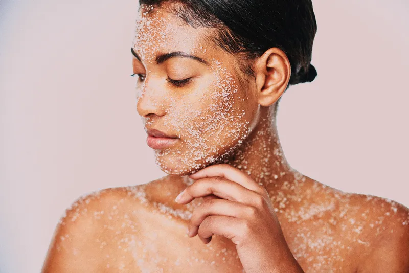 person with physical exfoliant on face and body