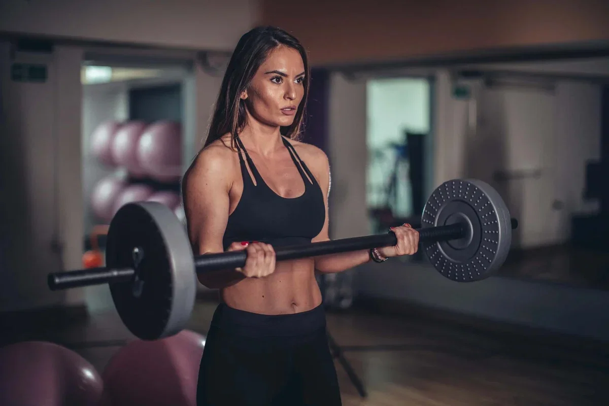 A picture of a woman working out in a gym curling dumbells. 