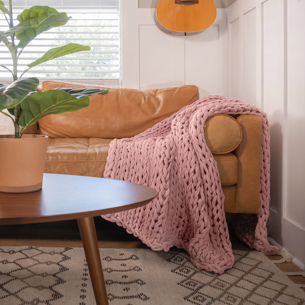 A pink knitted throw blanket draped over a light brown couch.