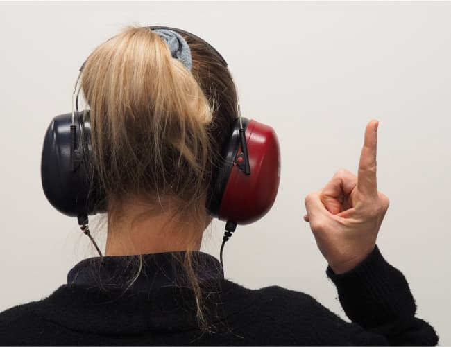 A woman wearing over-the-ear headphones holds one finger in the air.