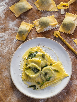 A plate of ravioli, with uncooked ravioli parcels and flour surrounding the plate
