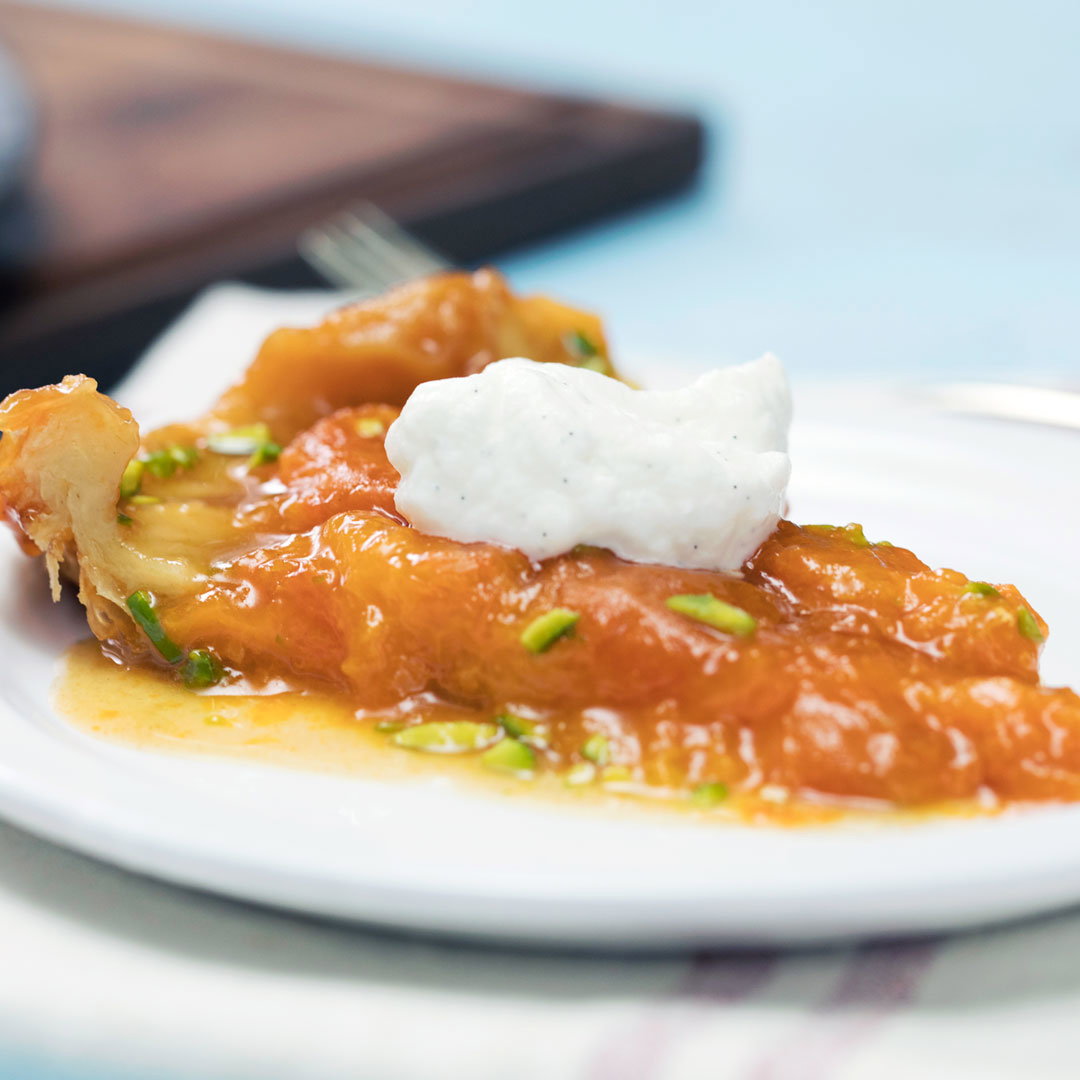 a plate with a slice of an orange apricot tarte dessert on it, topped with whipped cream