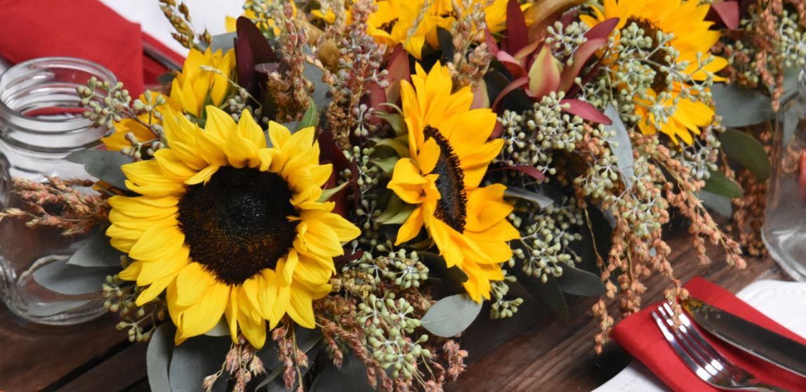Sunflowers and leafy stems in a floral arrangement on a wooden table with red napkins.