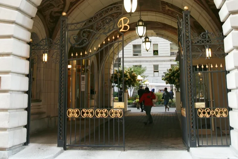 white stone arch entryway of the Belnord, where Martha Stewart and her daughter just purchased a unit; black iron gates with gold accents, gold “B” at center