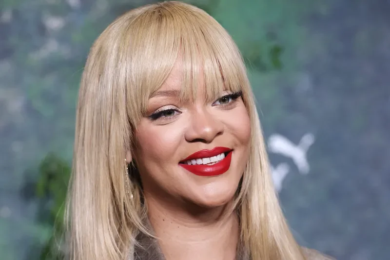Rihanna with blonde hair and bangs wearing pale brown outfit, smiling