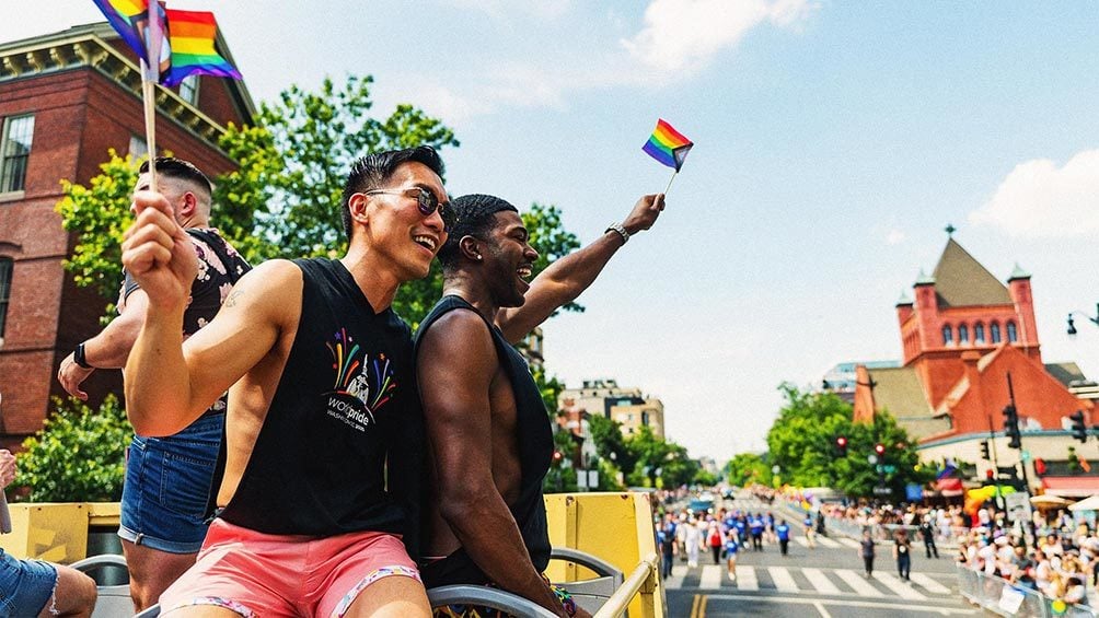 Image description: Two people waving flags during pride parade, in Washington, D.C.
