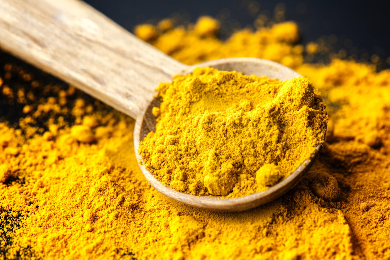 Close up of a pile of turmeric powder spread out with a wooden spoon in the middle of the pile with turmeric powder in the spoon