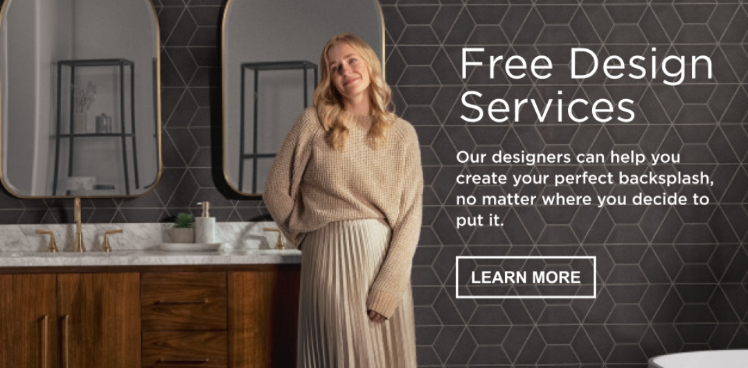 Woman smiling in bathroom with black geometric backsplash, double vanity with wood base and marble top, two gold faucets, and two gold mirrors. Text banner: free design services, our designers can help you create your perfect backsplash, no matter where you decide to put it.