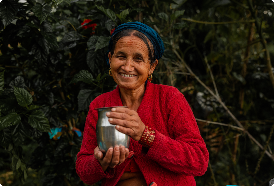 A Nepalese woman holds a cup of clean water while smiling.