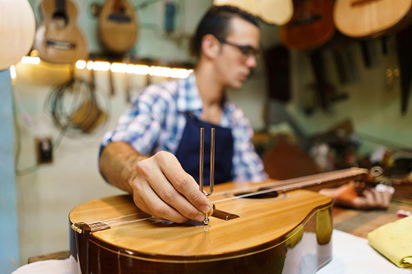 A luthier in a workshop tuning a classical guitar using a tuning fork on the body 
