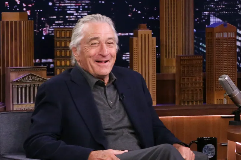 Robert De Niro on late night interview show sitting on chair laughing