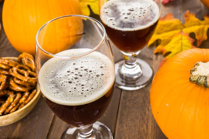two beer glasses on a table with pumpkins