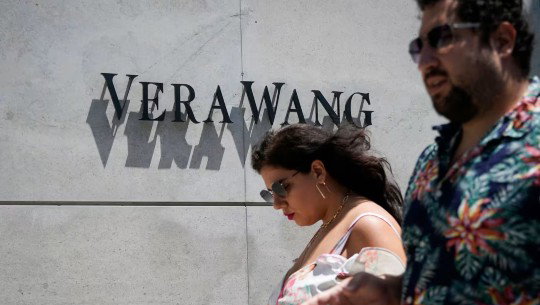 A man and woman pass in front of a Vera Wang logo on a store exterior