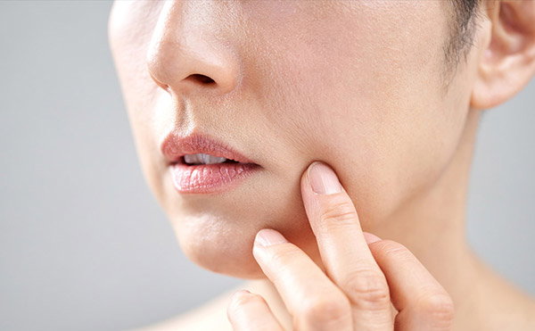 Close up view of a woman touching the skin on her cheek.