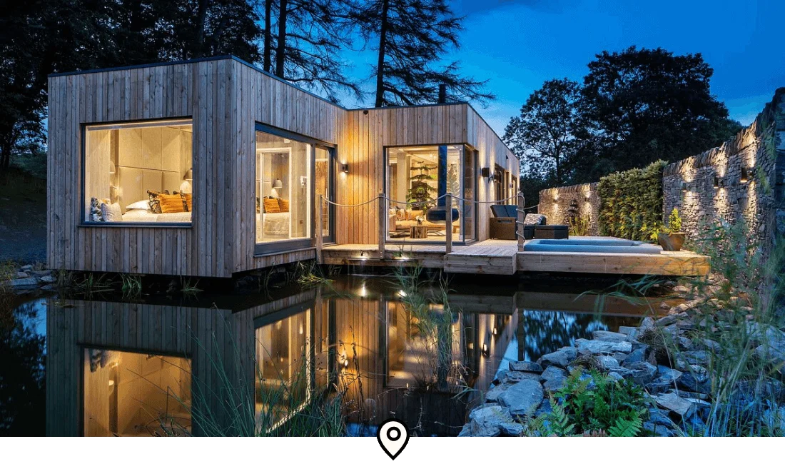 Image Description: Exterior of a sleek, rectangular wooden cabin built atop a lake at Gilpin Hotel & Lake House in Lake District, England
