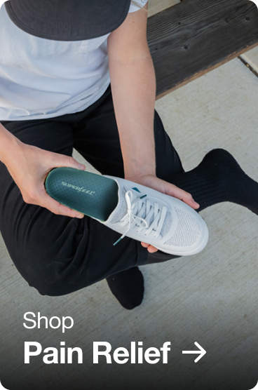 Person sitting on bench with leg crossed while inserting an insole into their white shoe.
