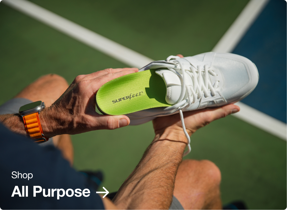 Person on a tennis court inserting a green insole into their white shoe.