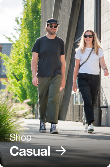 Couple walking down a sidewalk together, wearing casual clothes and sneakers.