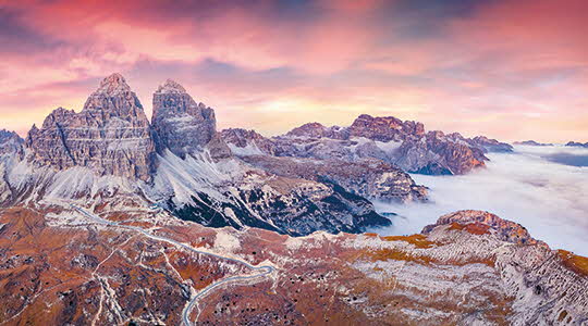 Montagnes rocheuse légerement enneigées, de couleurs rouges ou marrons dans les nuages