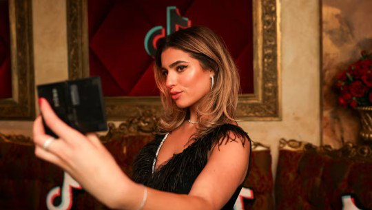 A woman poses in front of a TikTok logo in a frame on the wall