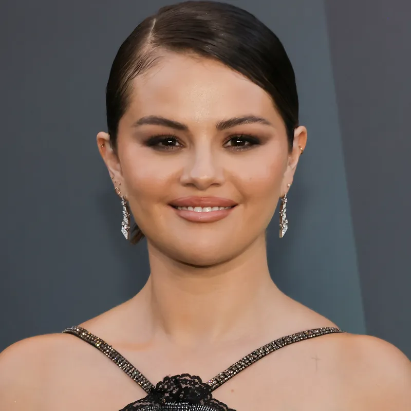 Selena Gomez appears at an awards show in a black gown and slicked-back hairstyle.