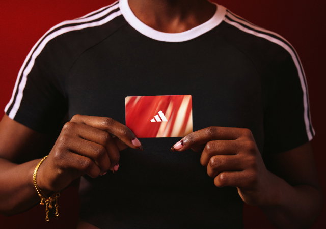 Person holding a red adidas gift card in front of a red backdrop