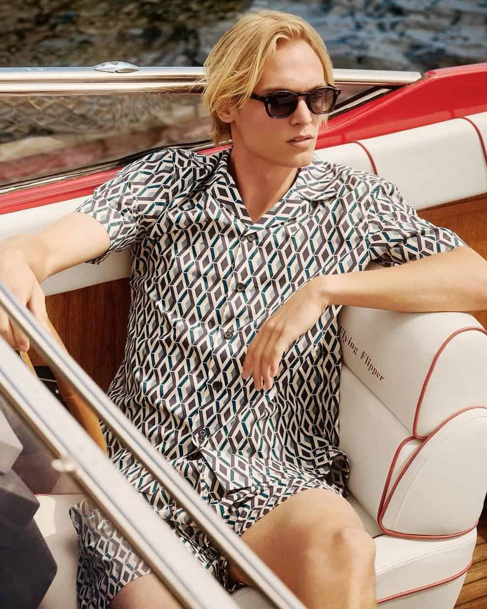 a woman wearing a black and white patterned shirt and shorts sitting in a boat