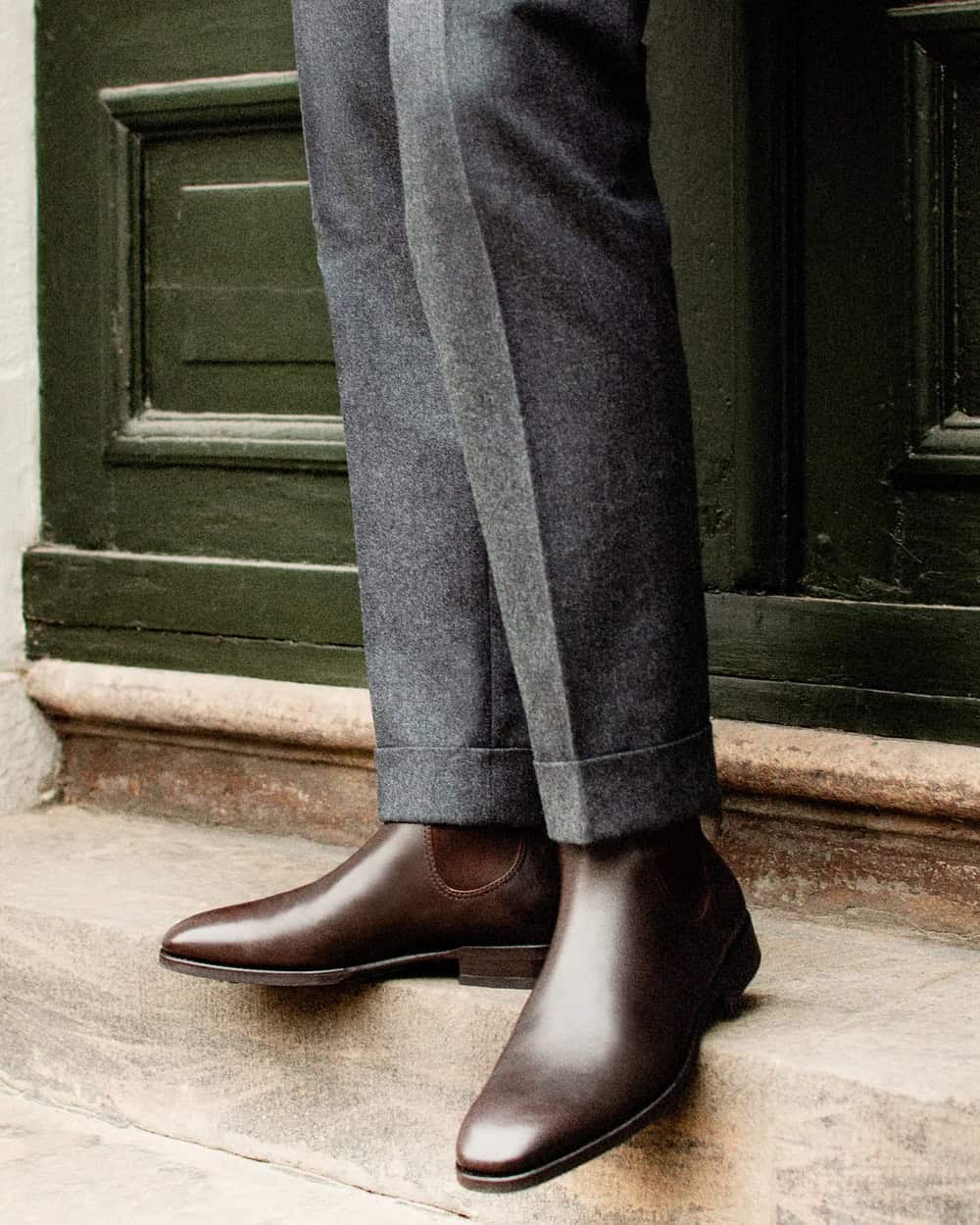 a man wearing grey trousers and a pair of brown shoes