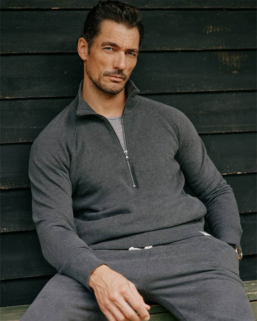 a man sitting on a bench wearing a sweatshirt and trousers