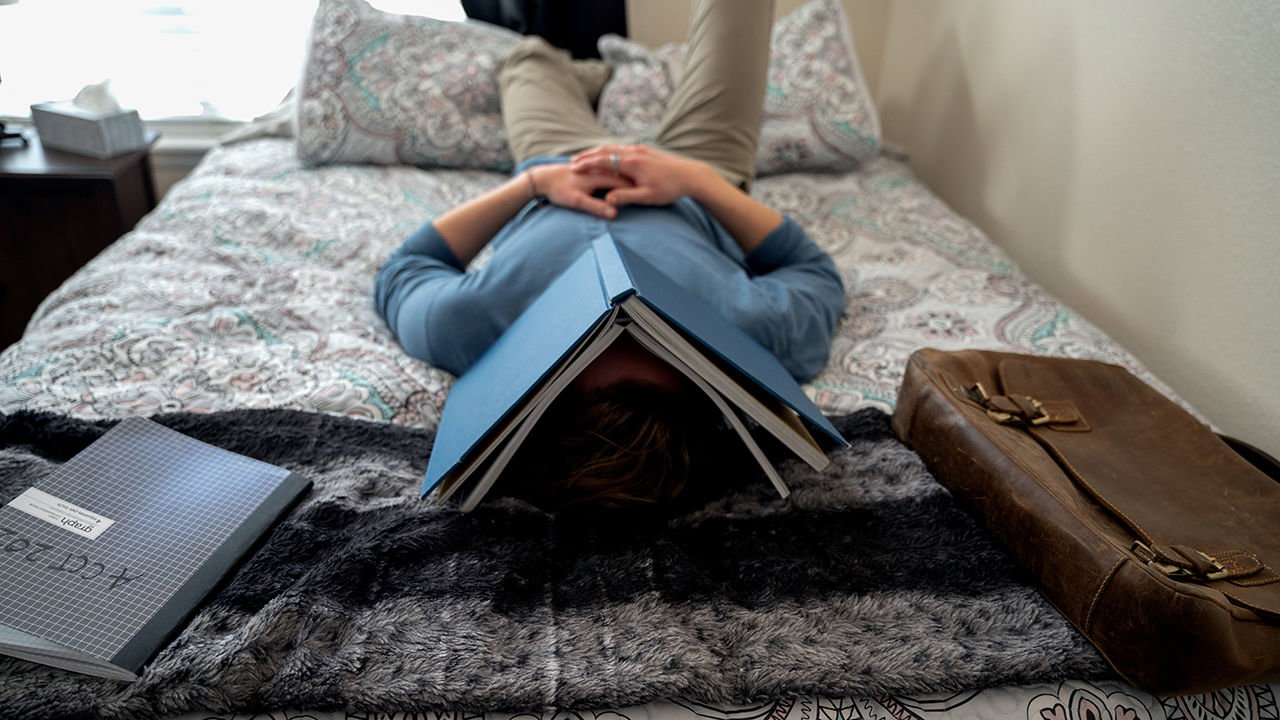 College student lying on bed with book over his head