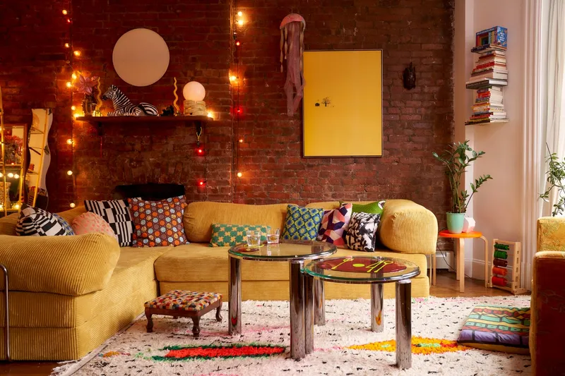 Yellow corduroy couch against a brick wall surrounded by colorful decor.