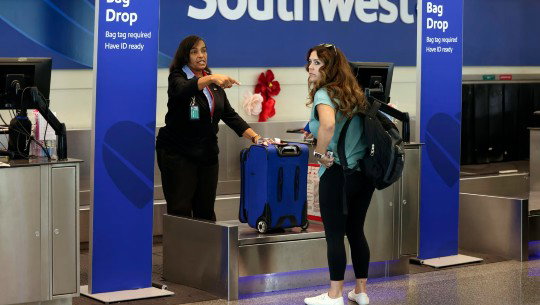 A traveler drops her suitcase with Southwest employees at the airport
