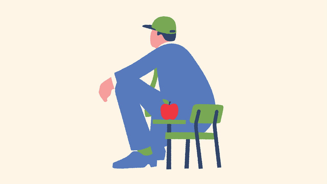An adult wearing a cap sat in a small school desk