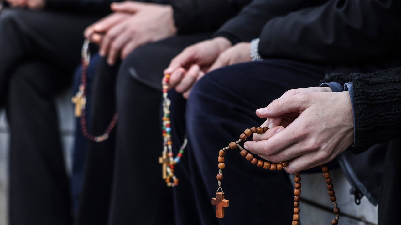 A close up of a few Rosaries and pairs of hands in prayer.