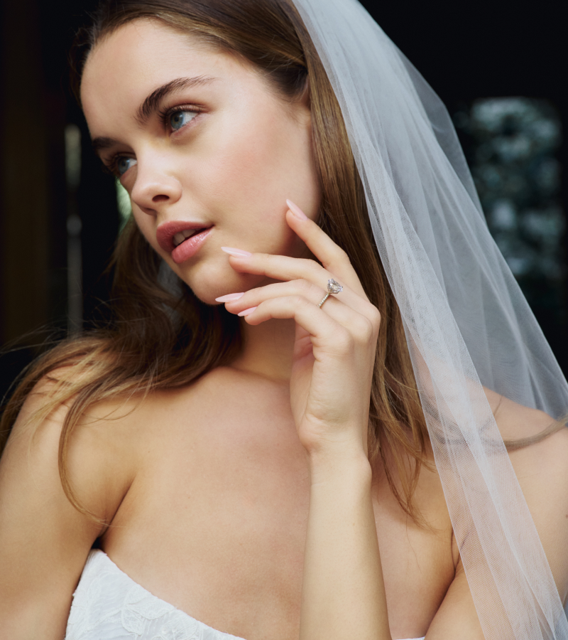 A bride holds her left hand up to her face to reveal a stunning engagement ring