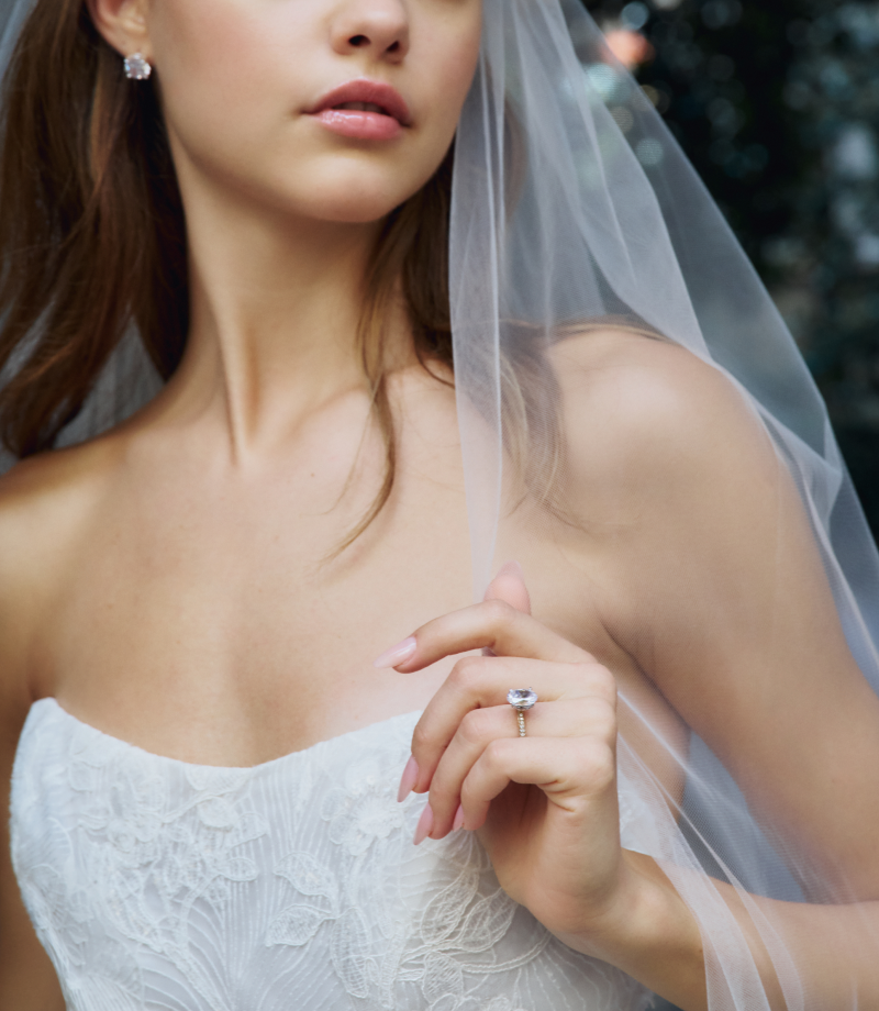 A bride holds her left hand up near her chest to reveal a stunning engagement ring