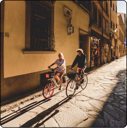 Image Description: A man and a woman on bikes riding through a cobblestoned street at sunset.