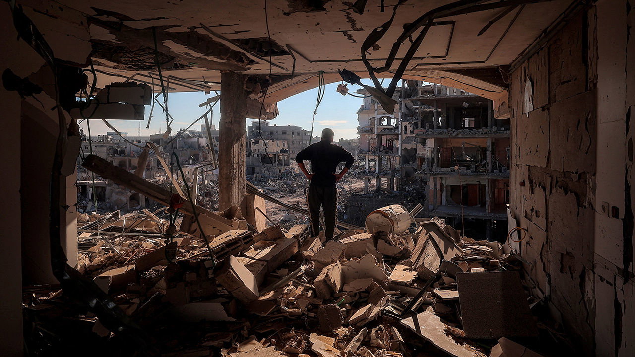 A man stands on an elevated floor in a heavily-damaged building without walls in Rafah