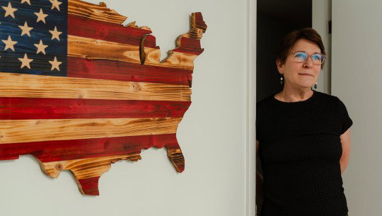 Dianna Huff next to a wall-mounted wood cutout in the shape of the United States and painted with the American flag