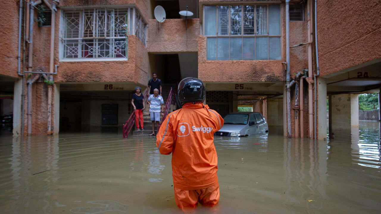 A Swiggy food delivery person wades through floodwaters to deliver an order.