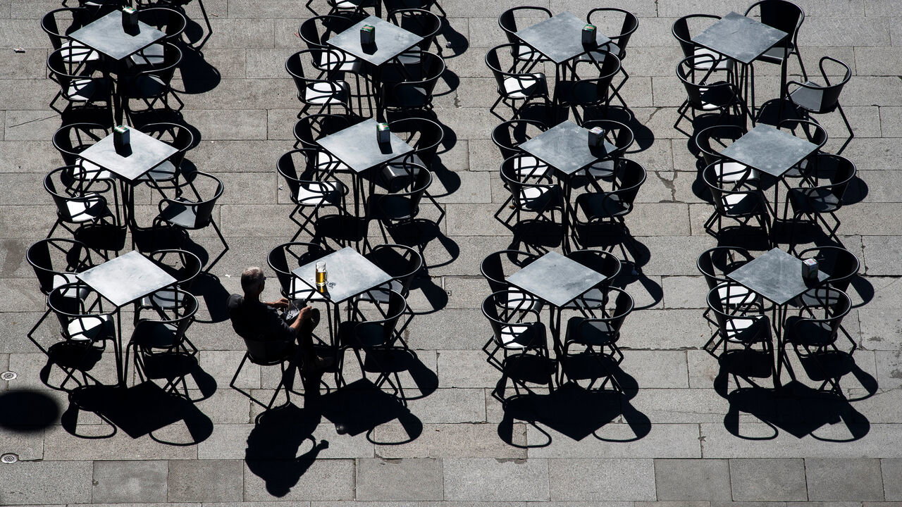 A lone man sits with a beer, at one of many cafe tables in a square in downtown Porto, Portugal.