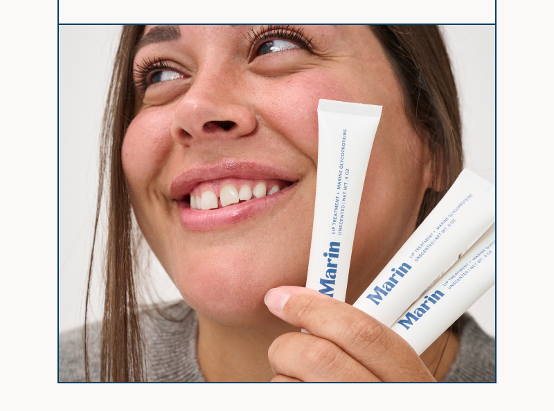 Close-up of Amber holding three Marin lip treatment tubes near her cheek, showcasing soft lips and glowing skin.