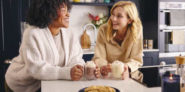 Two friends chatting and drinking hot chocolates in the kitchen