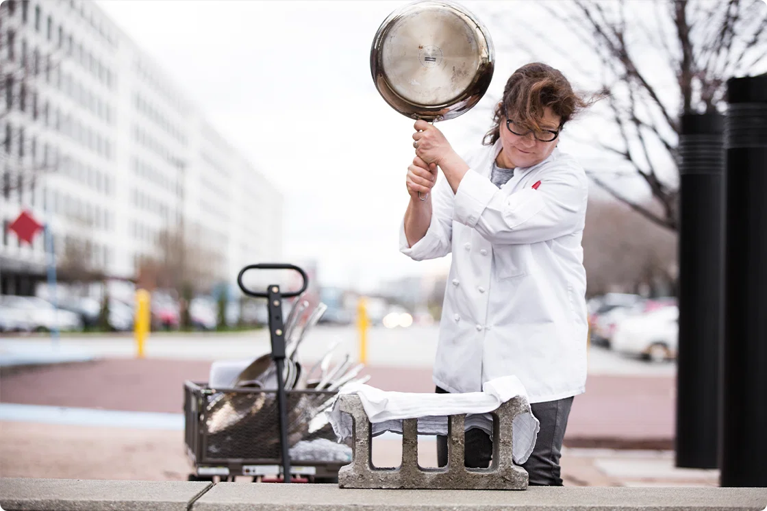 Lisa McManus testing the durability of stainless-steel skillets by whacking them on a concrete block.