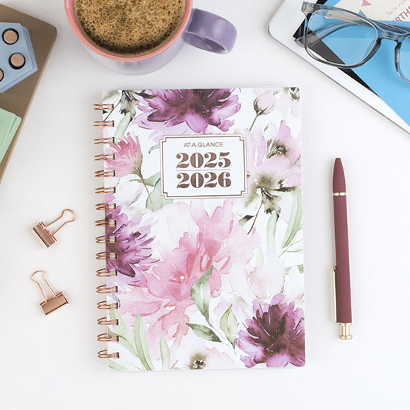 Floral planner next to a pen, clips, coffee cup and glasses 