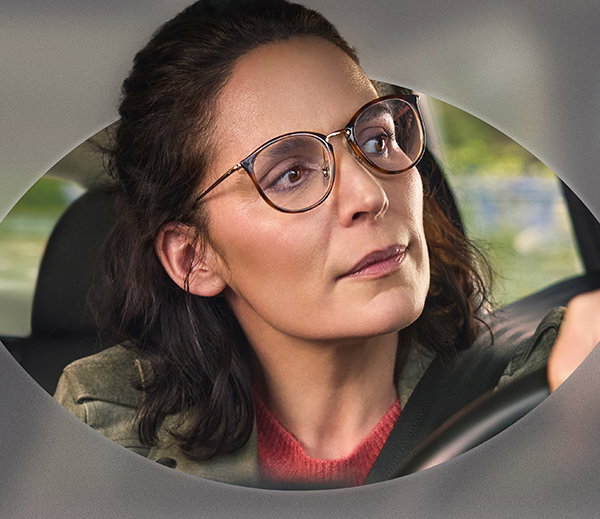 Frau mit Brille hinter dem Steuer eines Autos.
