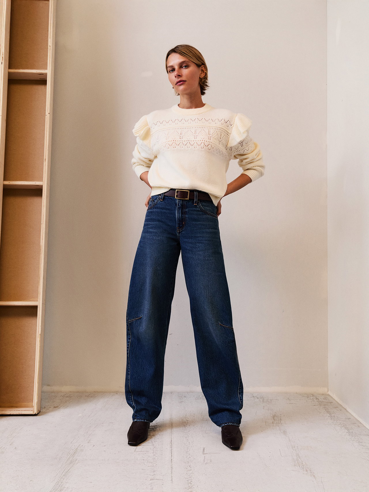 Woman wearing a white sweater and dark wash jeans.