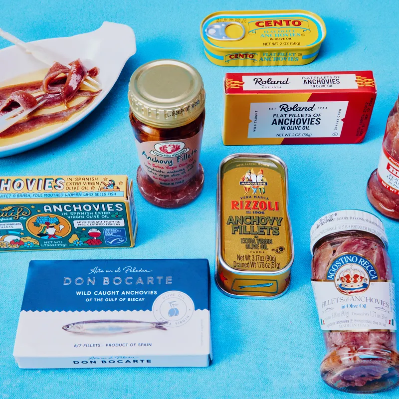 A variety of anchovy tins and jars on blue background. 