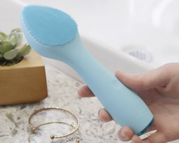 Blue facial exfoliating device with a bathroom counter in the background